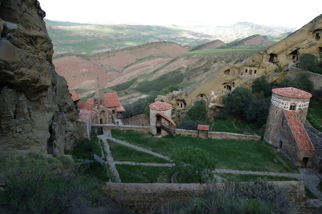 David Gareja Lavra monastery buildings and cave cells set against rolling desert hills.