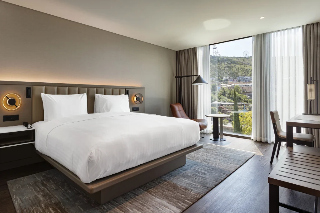 ART Riverfront Hotel Tbilisi — Modern hotel room with king bed, large window, and city view.
