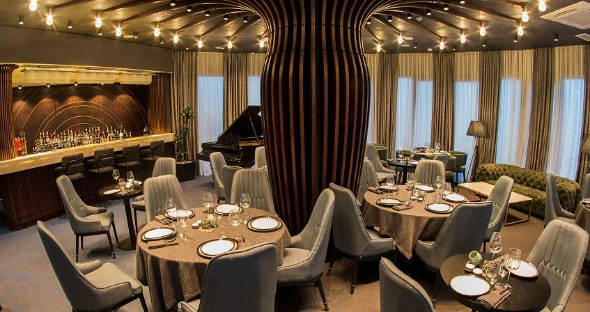 Adamo — Elegant restaurant with bar, piano, and candlelit tables set for dining.