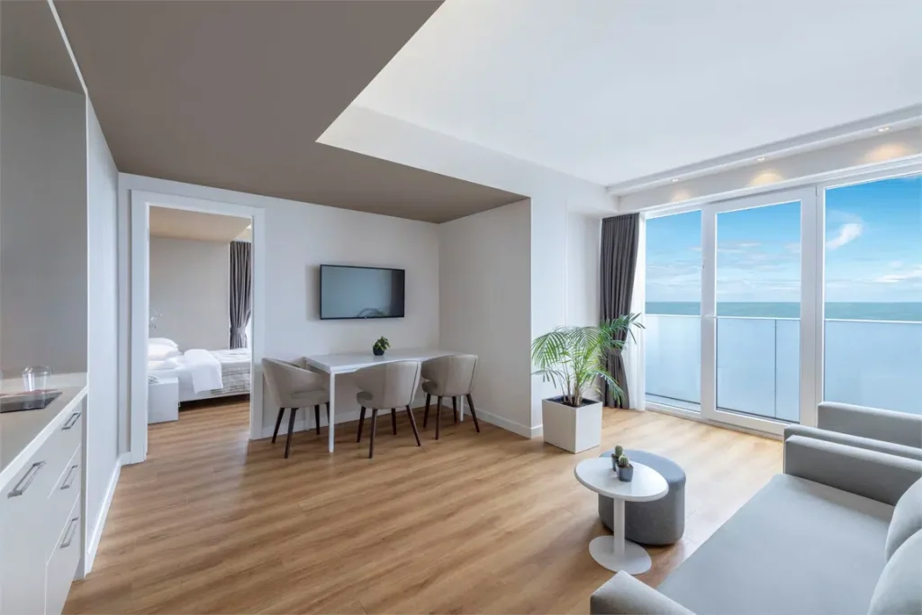 Alliance Palace — Spacious suite living area with sofa, dining table, and floor-to-ceiling sea-view windows.