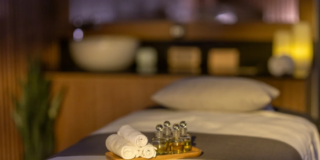 Ambassadori Goderdzi — Spa treatment table with rolled towels and massage oils in dim lighting.