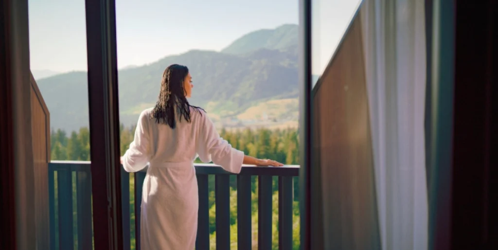 Ambassadori Goderdzi — Guest in robe admiring a mountain and forest view from a balcony.
