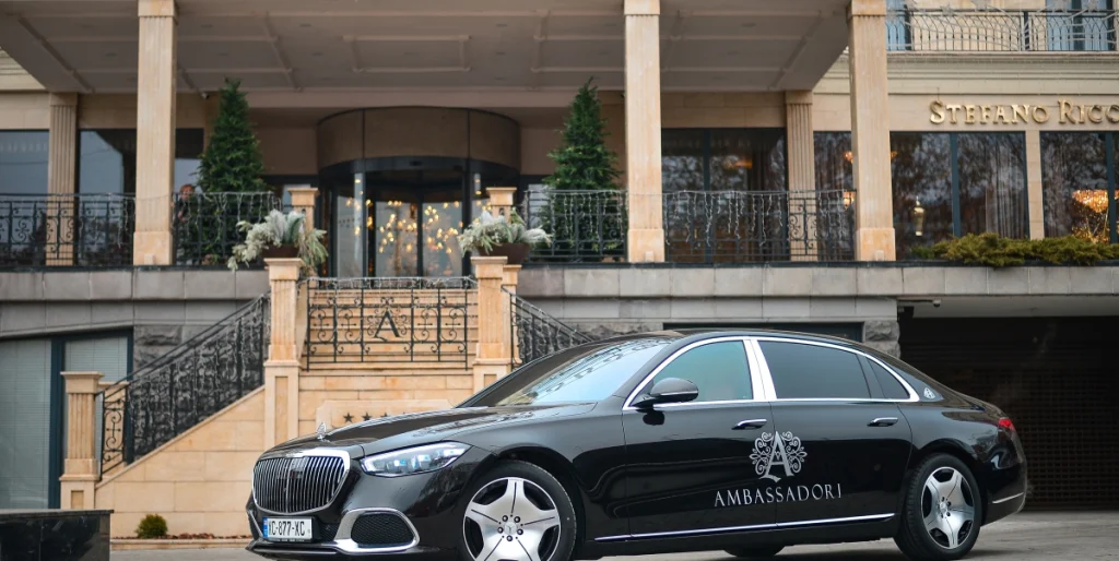 Ambassadori Tbilisi — Hotel entrance facade with columns and a luxury car parked outside.