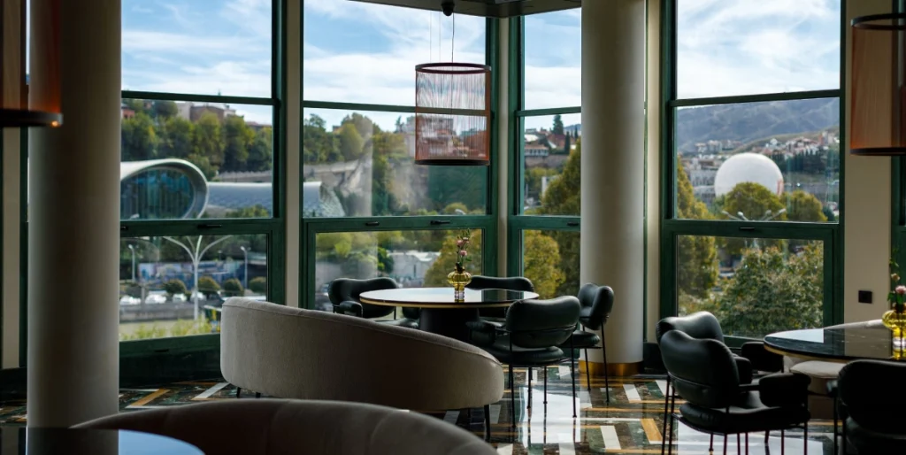 Ambassadori Tbilisi — Lounge seating area with large windows overlooking the river and city.