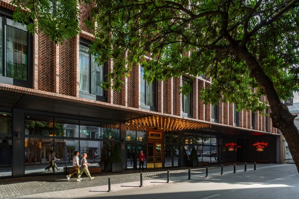 Artizan Design Hotel ® — Brick facade entrance of the hotel with illuminated marquee sign and tree-lined street.