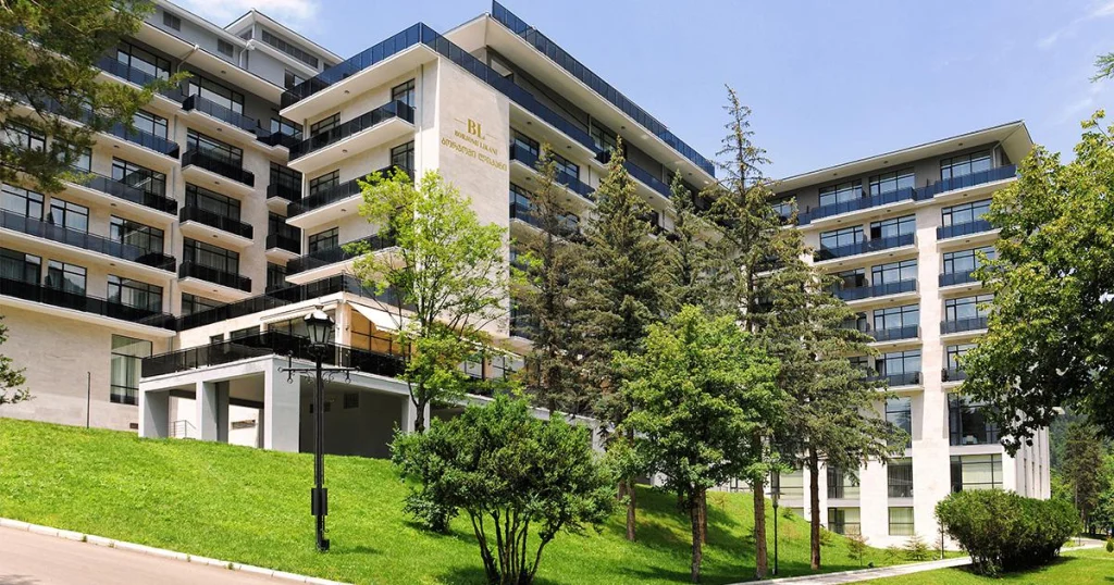 Bagrationi — Modern multi-story hotel building surrounded by green trees and lawn under a blue sky.