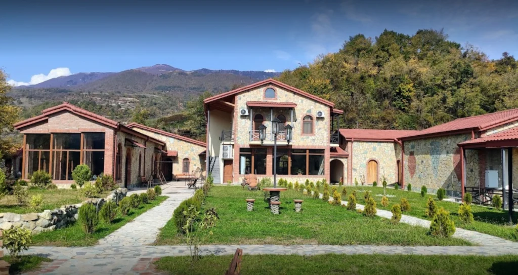 Barakoni Winery — Stone-built winery building with red roofs set against green hills and lawn.