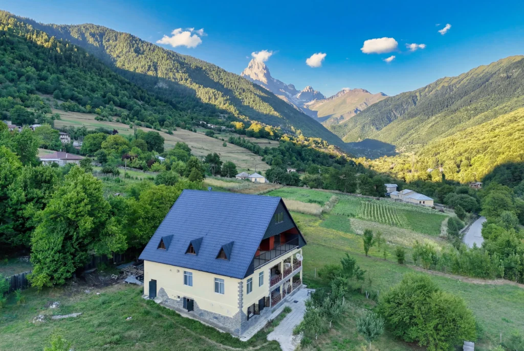 Becho House — Aerial view of the house with mountain peak and green valley backdrop.