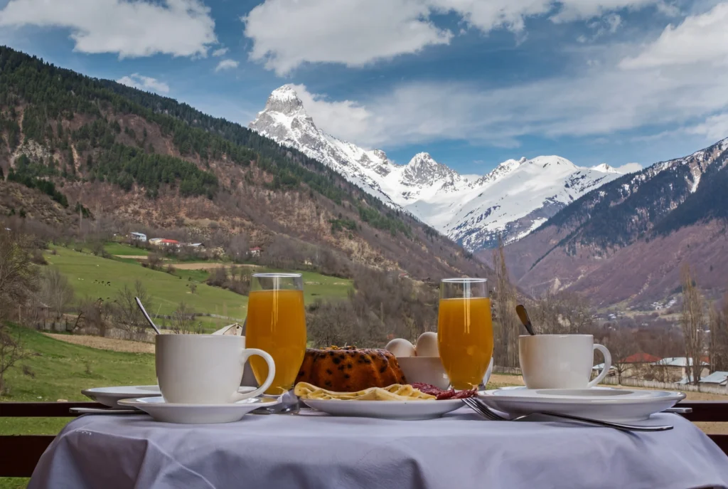 Becho House — Breakfast table set outdoors with snow-capped mountain view in background.