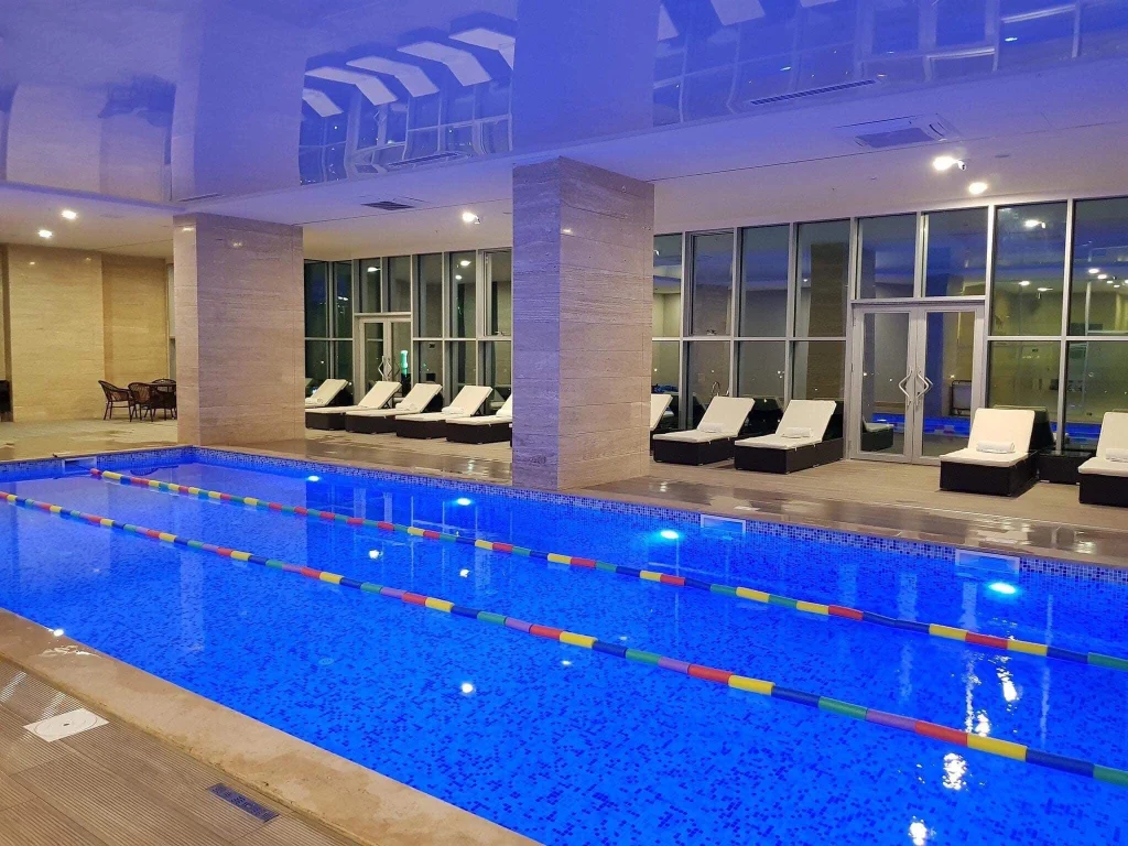 Best Western Premier Batumi — Indoor swimming pool with lane markers and poolside lounge chairs lit at night.