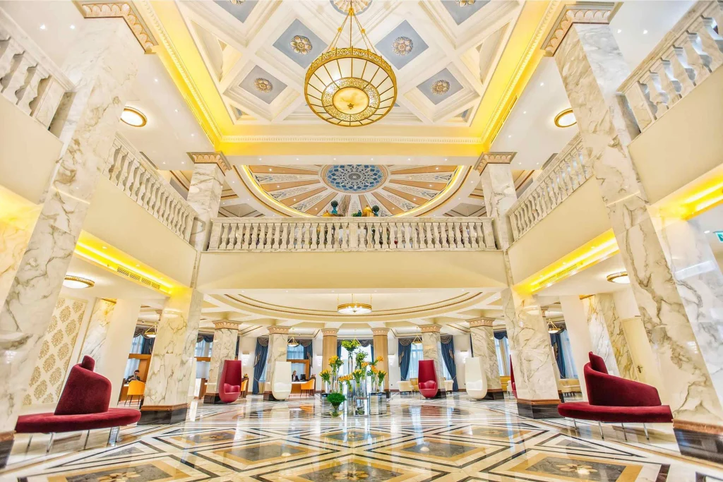 Biltmore Tbilisi Hotel — Grand marble lobby with ornate ceiling, chandelier, and red upholstered seating.