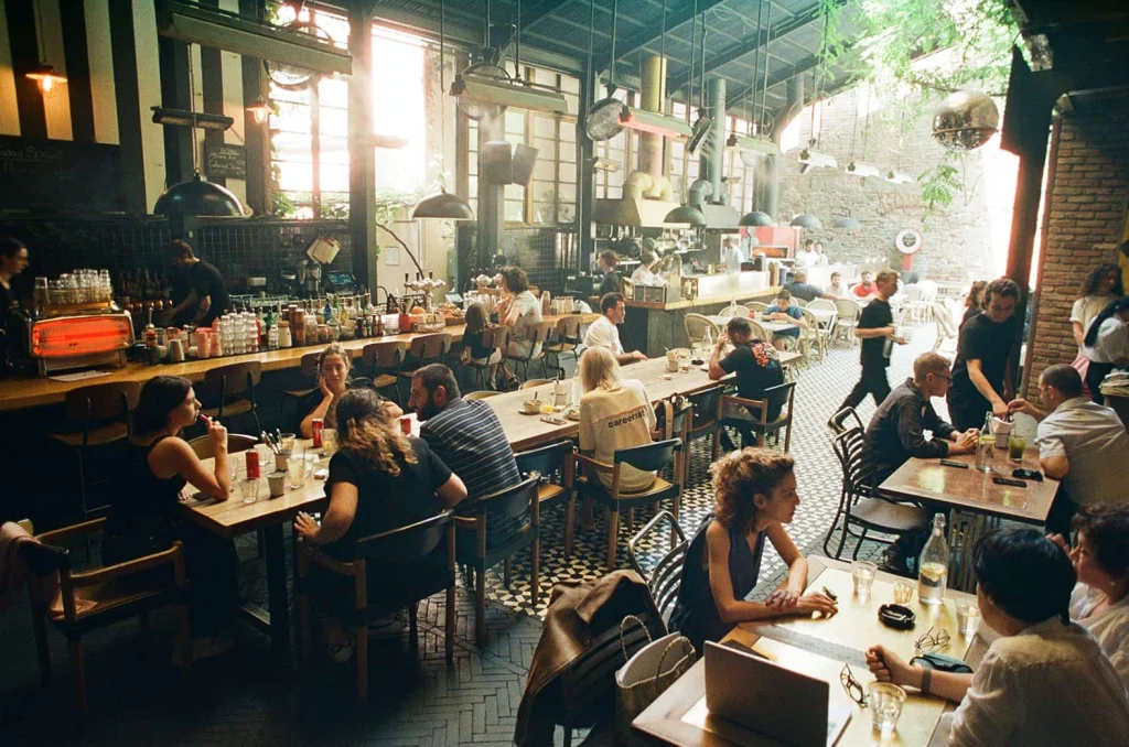 Blueberry Nights Hotel — Lively indoor restaurant space with a long bar, pendant lighting, and seated guests.