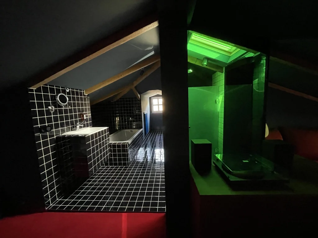 Blueberry Nights Hotel — Attic-style suite with black tiled bathroom, tub, and green-lit glass shower nook.