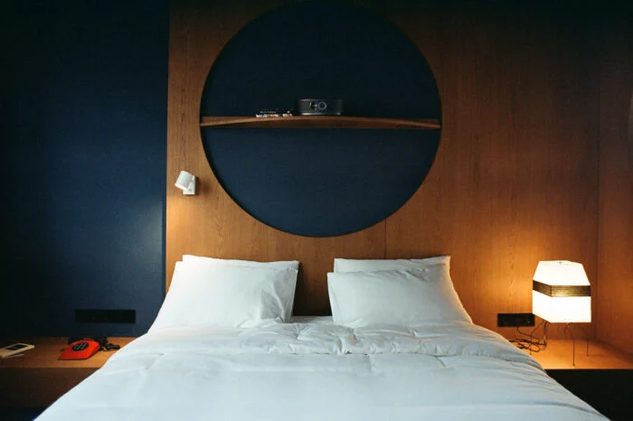 Blueberry Nights Hotel — Hotel bed with white linens set against a dark blue wall and circular wood shelf.