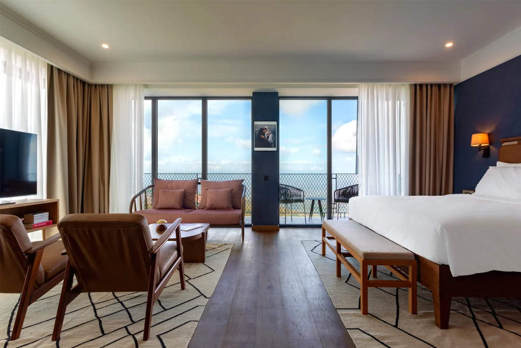 Bodbe Hotel — Hotel room with king bed, seating area, and large windows overlooking the sea.