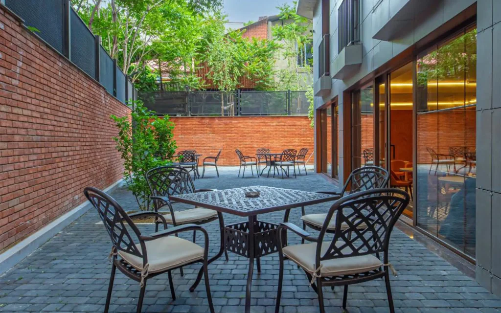 Boutique Hotel Calligraphy Tbilisi — Outdoor courtyard seating area with tables and chairs surrounded by brick walls and greenery.