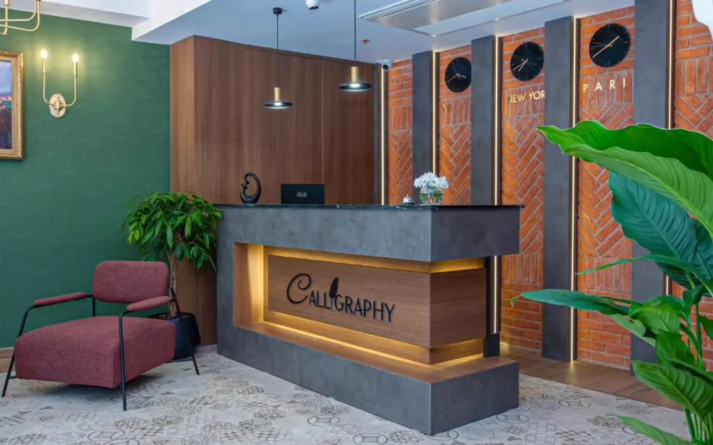 Boutique Hotel Calligraphy Tbilisi — Hotel lobby reception desk with decorative wall clocks and green accent wall.