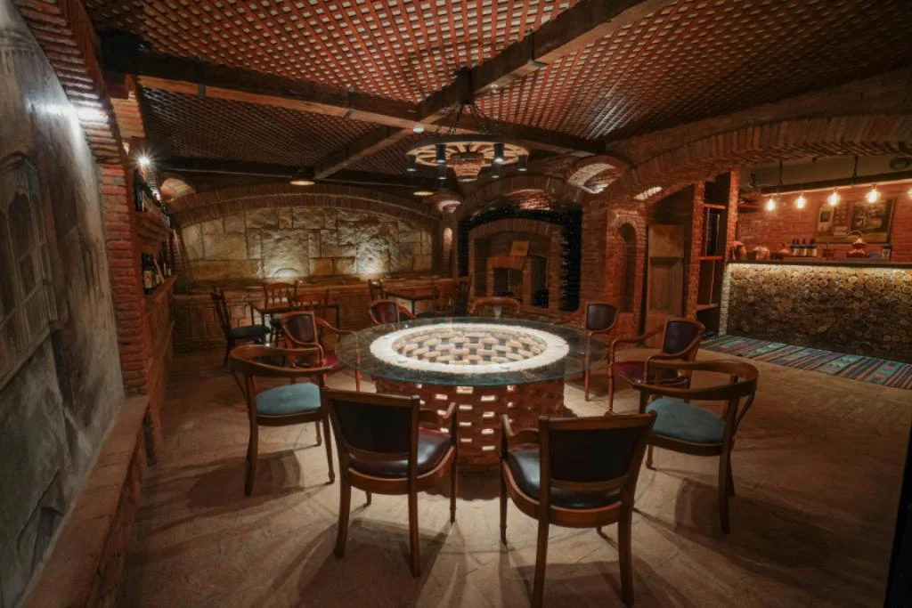 Boutique Hotel Kviria — Vaulted brick cellar lounge with round table and wine storage niches.