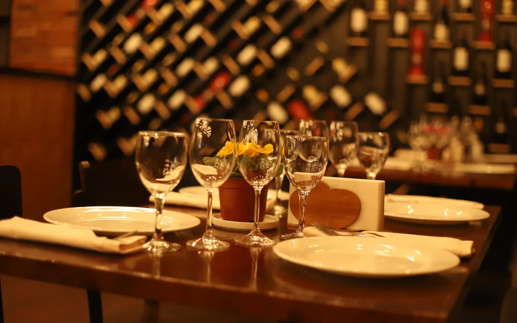 Bricks Hotel — Restaurant table set with wine glasses and plates in front of a wine rack wall.
