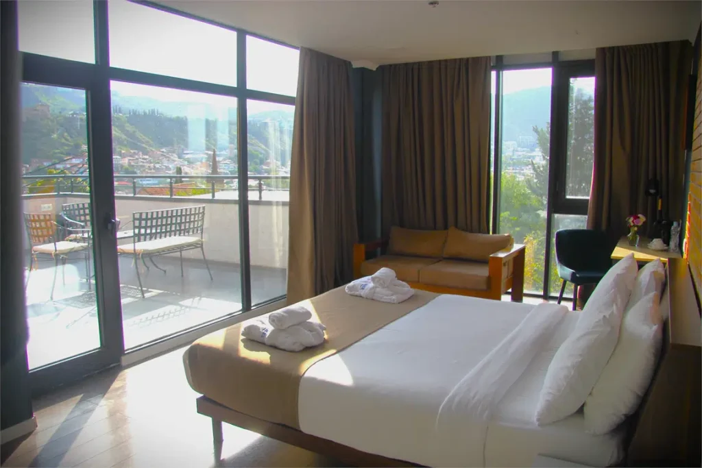 Bricks Hotel — Hotel room with large windows opening onto a balcony overlooking the city and hills.