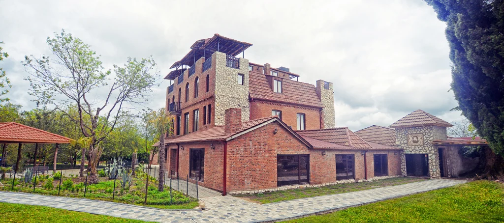 Chateau Chikovani — Brick and stone chateau building with tower, surrounded by a landscaped garden.