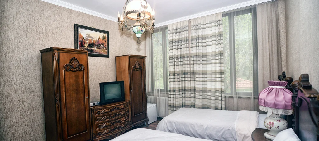 Chateau Chikovani — Twin bedroom furnished with antique wooden wardrobes and patterned curtains.