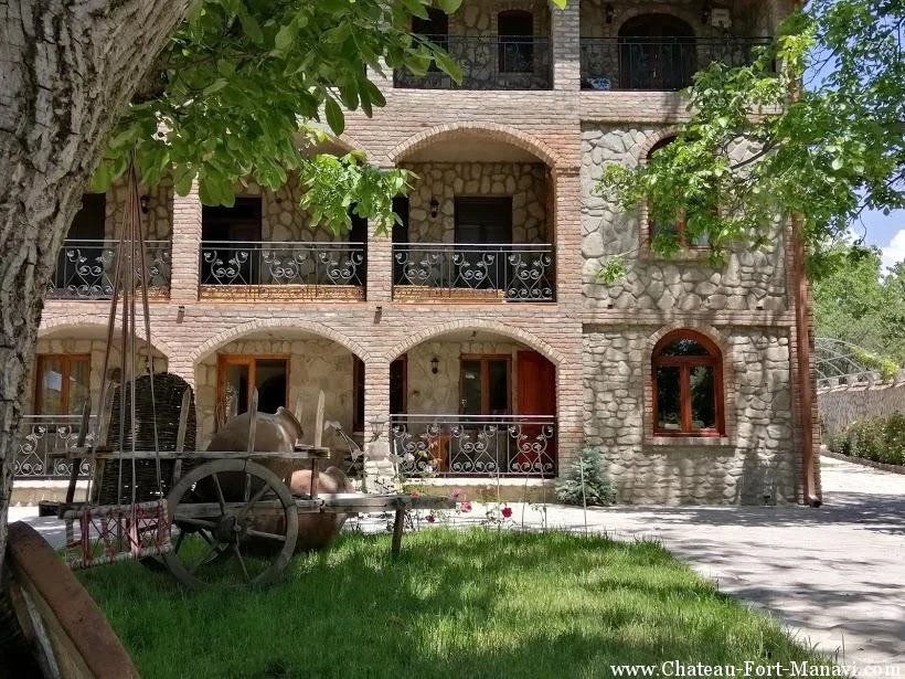 Chateau Fort de Manavi — Daytime view of the stone courtyard facade with arched balconies and garden.