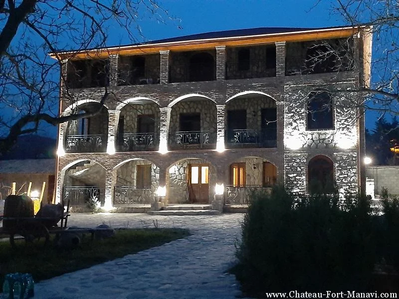 Chateau Fort de Manavi — Stone chateau building with arched balconies illuminated at night.