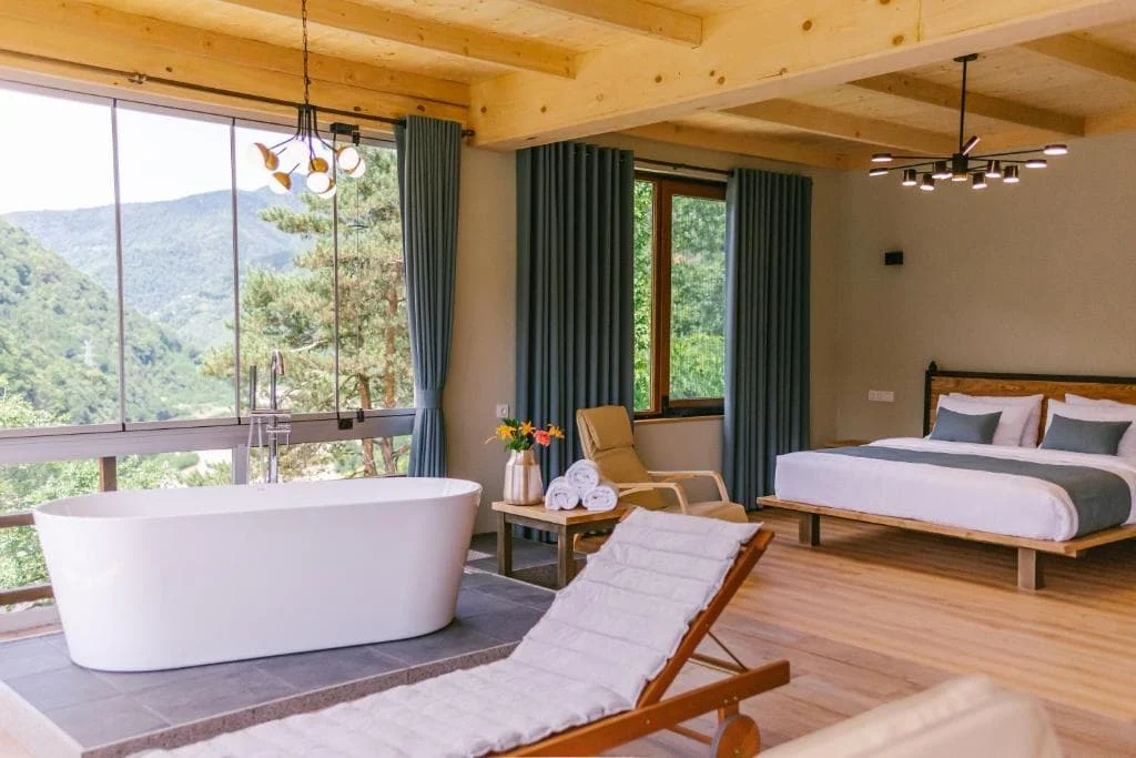 Chateau Iveri — Spacious room with freestanding tub, bed, and large windows overlooking mountains.