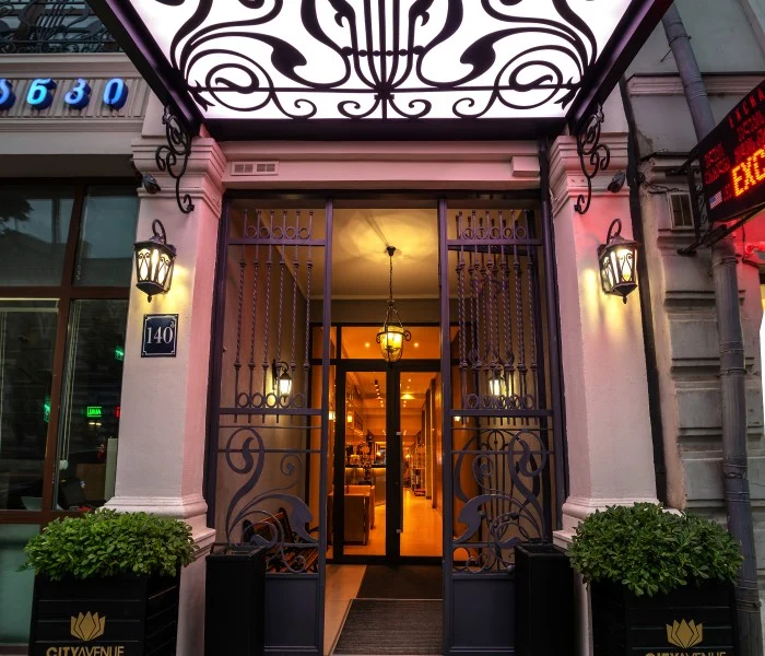 City Avenue Hotel — Ornate entrance doorway of the hotel illuminated at dusk with decorative ironwork.