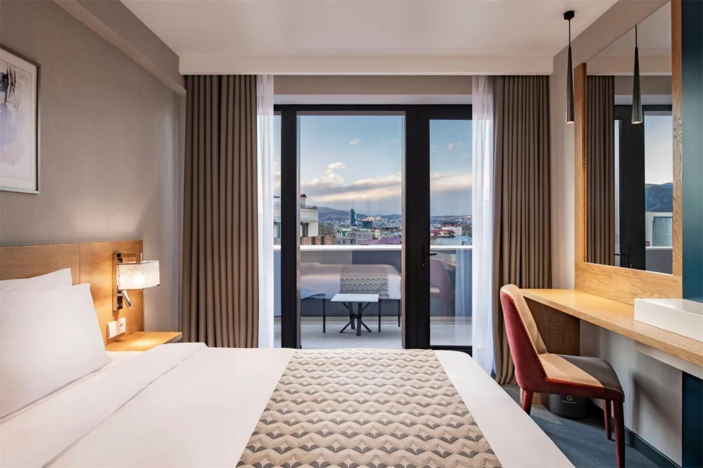 Clocks Hotel — Hotel room with a double bed and a private balcony overlooking the city skyline.