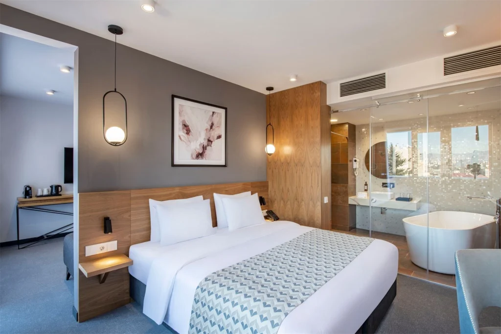 Clocks Hotel — Spacious suite with a freestanding bathtub open to the bedroom and city view windows.