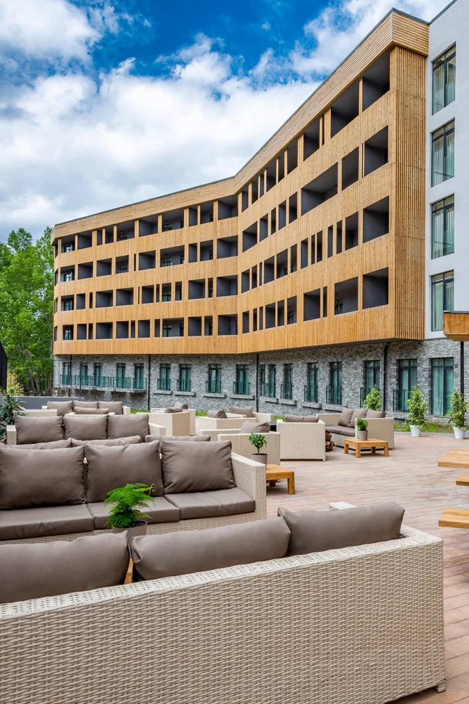 Dialog Kokhta Bakuriani — Hotel exterior with wooden facade and outdoor lounge seating area on terrace.
