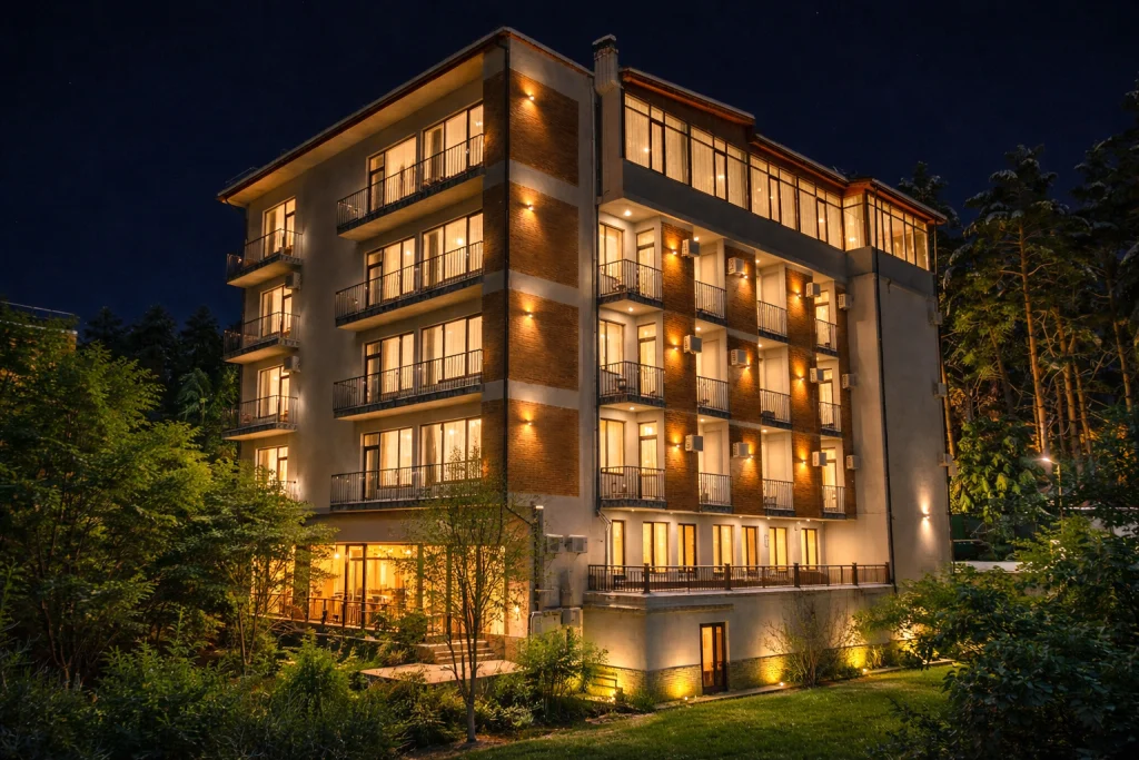 Emerald Borjomi — Night view of the hotel building with illuminated windows and balconies surrounded by trees.