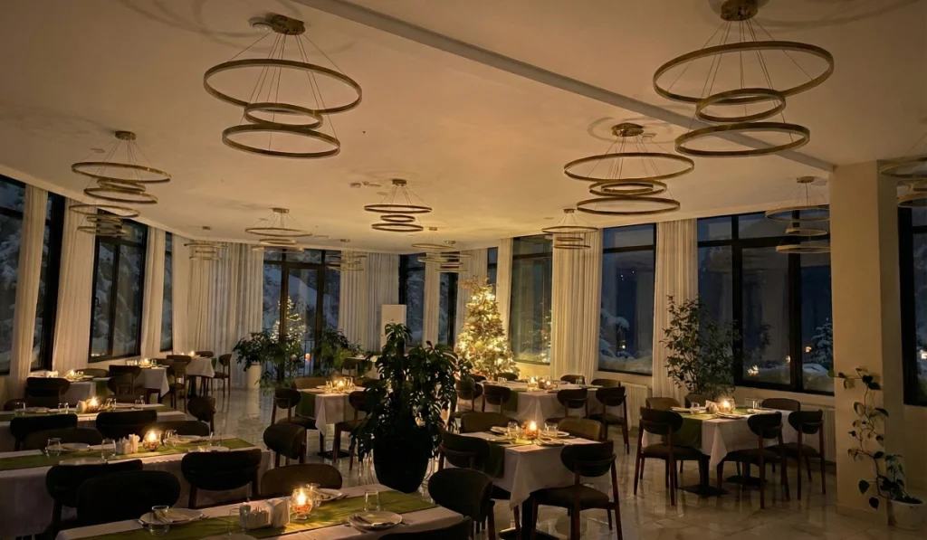 Emerald Borjomi — Elegant hotel restaurant with set tables, ring chandeliers, and large windows showing a night view.