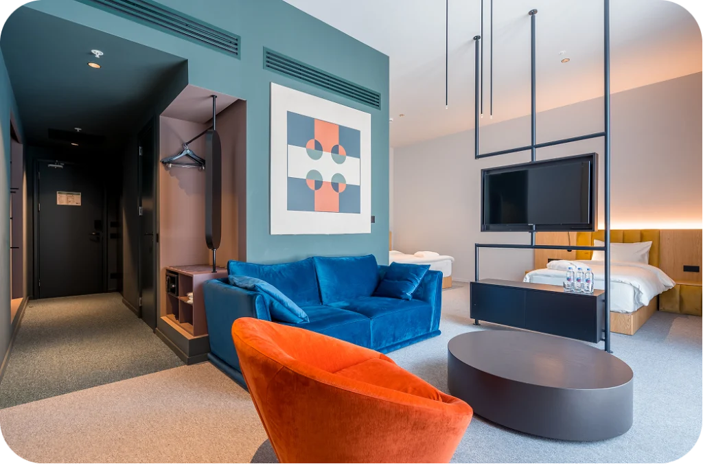 Episode Tbilisi — Modern suite with blue sofa, orange armchair, and colorful artwork near the bed.