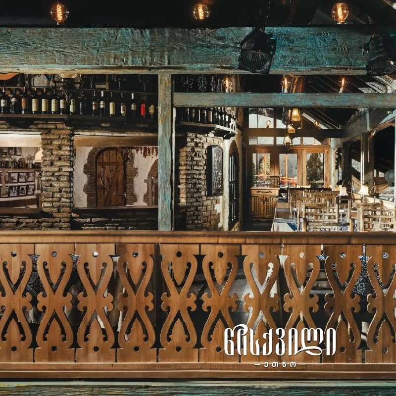 Ethno Tsiskvili — Rustic restaurant interior with stone walls, wooden beams, and a wine shelf bar.