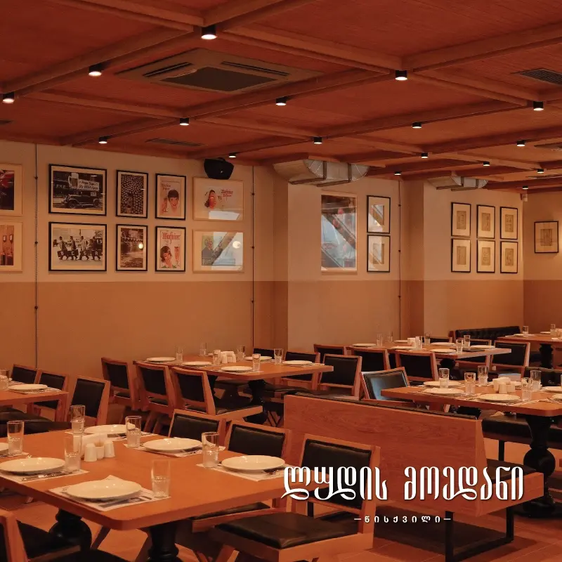 Ethno Tsiskvili — Wood-paneled dining room decorated with framed artwork and set tables.