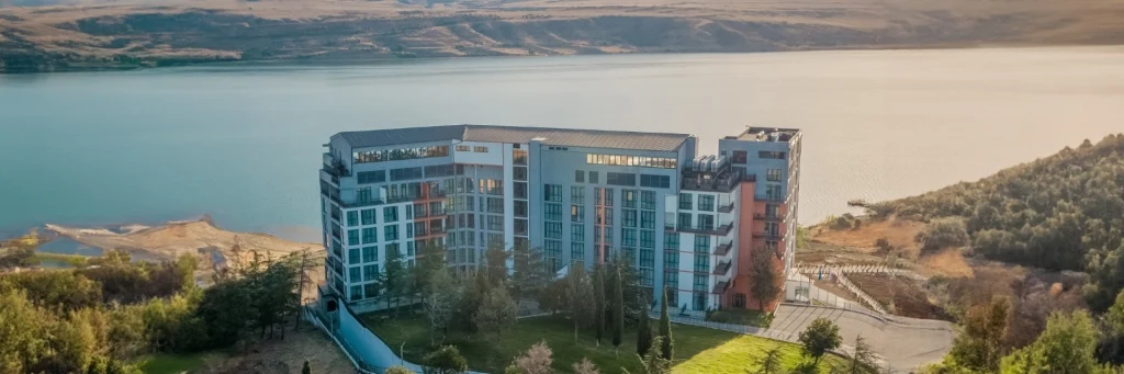 Gino Seaside Tbilisi, Trademark Collection by Wyndham — Aerial view of the hotel building situated beside a large reservoir lake.