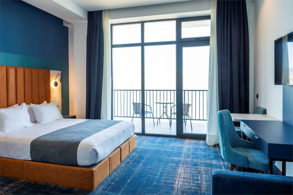 Gino Seaside Tbilisi, Trademark Collection by Wyndham — Hotel room with king bed, blue decor, and private balcony overlooking the water.
