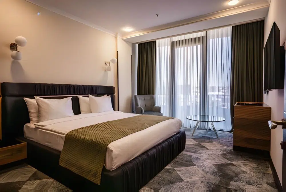 Gori Inn — Hotel room with a large bed, armchair, and curtained window overlooking the city.