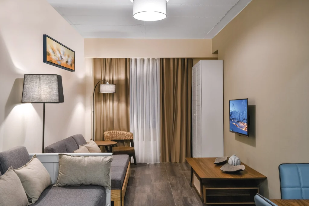 Gudauri Hills Apart Hotel — Living area apartment with sofa, TV, and curtained window.