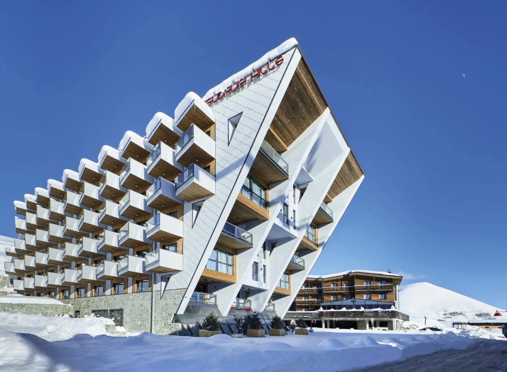 Gudauri Hills Residence — Distinctive angular hotel building exterior covered in snow with mountain backdrop.