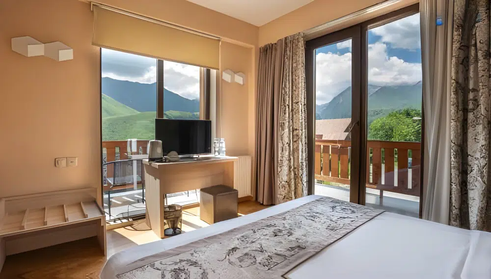 Gudauri Inn — Bedroom with balcony access offering mountain views, desk, and television.