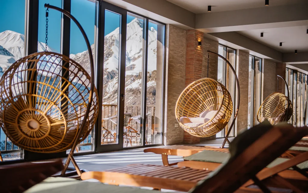 Gudauri Inn — Lounge area with hanging rattan chairs and sun loungers facing snow-capped mountain views.