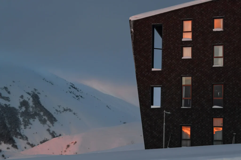 Gudauri Lodge — Hotel building exterior glowing at dusk against a snowy mountain backdrop.
