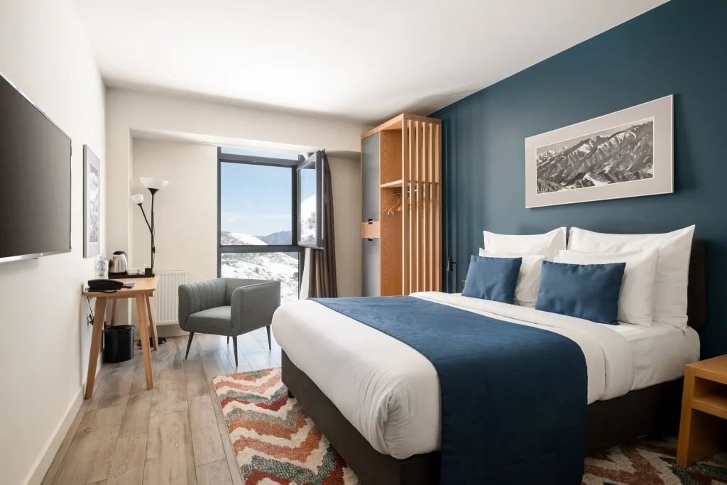 Gudauri Lodge — Hotel room with double bed, teal accent wall, and mountain-view window.