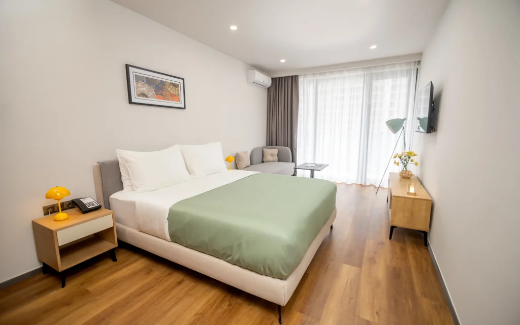 HOTEL BLUE SKY — Modern hotel bedroom with green bedspread, sitting area and large window.