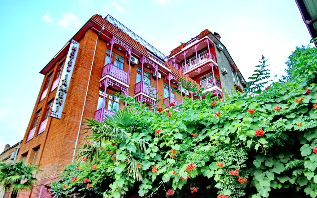 HOTEL IR-ME-NI — Brick hotel building with pink balcony railings viewed from below amid greenery.