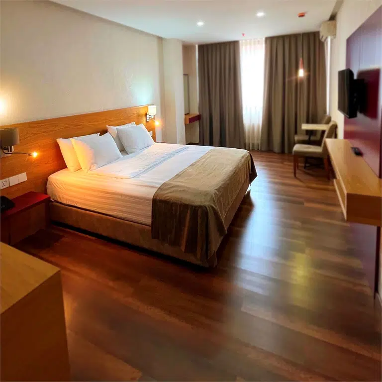 HOTEL IR-ME-NI — Hotel room with a large bed, wood flooring, and warm ambient lighting.